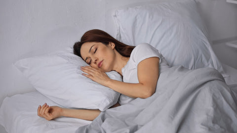 A young woman sleeping in a bed with white sheets on a Martex EcoPure Recycled Polyester Green Pillow from WestPoint Home.