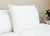 The Pillow Factory Housekeeper's Choice Heavenly Spiral Pillow, featured at many Borgata Hotel Casino & Spa® locations, sits upright against a beige wall on a neatly made bed with white bedding, creating a calm and inviting atmosphere.