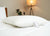 The Pillow Factory Housekeeper's Choice Heavenly Spiral Pillow, featured at many Borgata Hotel Casino & Spa<sup>®</sup>, rests on a white bed, with a tag attached. A tripod floor lamp and green plant create a cozy, upscale hotel-like ambiance.