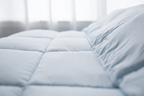 A close up of a blue Pillowtex hypoallergenic comforter on a bed.