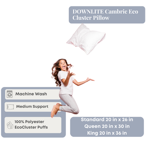 Joyful woman in loungewear appears to be mid-jump with a Downlite® Cambric Eco Cluster Pillow floating beside her, highlighting its machine washability, medium support, and eco-friendly materials.