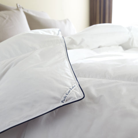 A Pacific Coast Feather SuperLoft™ Down Comforter by Pacific Coast Feather Company on a bed with a white comforter and a blue pillow.