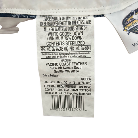 Close-up of a white garment label with black text detailing the Pacific Coast Feather Down Chamber Pillow's material composition, care instructions, and manufacturer information for the Pacific Coast Feather Company, including the address in Seattle, WA.