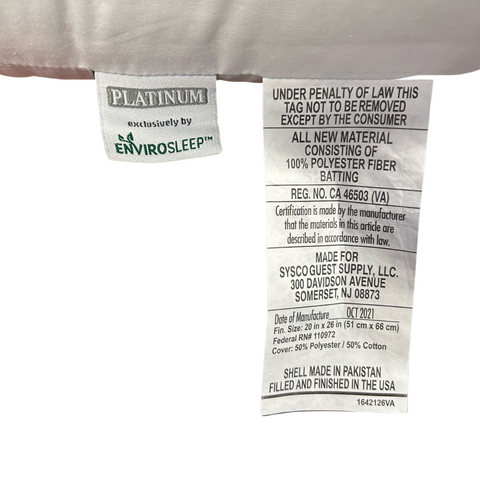 Close-up of two clothing labels showing brand and care instructions. The left label features "exclusively by Manchester Mills," right label includes material details and manufacturing info, emphasizing "made in the Envirosleep Platinum Garneted Polyester Fiber Fill Pillow.