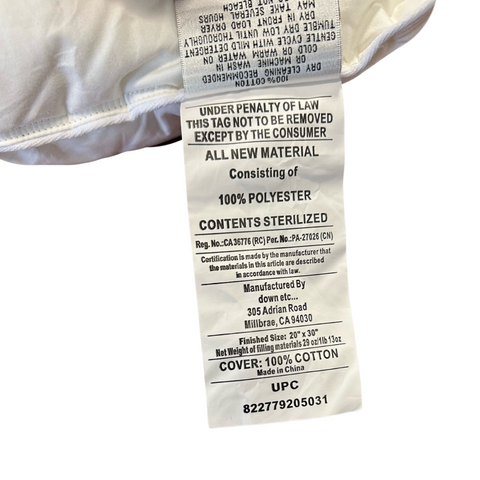 A close-up of a clothing label showing text that includes care instructions, fabric composition (100% siliconized polyester), and manufacturing details. It is attached to a white garment with visible stitching of the Down Etc. Fairfax Pillow - Featured at St. Julien Hotel & Spa<sup>®</sup> by Down Etc.