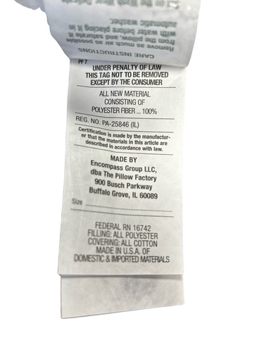 A close-up of a crumpled care label, displaying material content, compliance with law, and manufacturer details of a Brilliance Gel Fiber Pillow by Pillow Factory, with blurred text indicative of the tag's fabric texture.