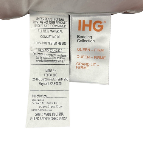 Close-up of a white Holiday Inn Infinity Pillow | Extra-Firm Support tag from the Keeco bedding collection showing text that specifies material content as 100% polyester fibers, made by Kadeco, LLC. It includes manufacturer details, product size for