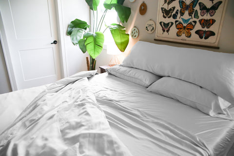 A white bed with Pillowtex Copper Infused Bamboo Sheet Set | Antimicrobial, Cooling, and Breathable sheets and a plant on it.