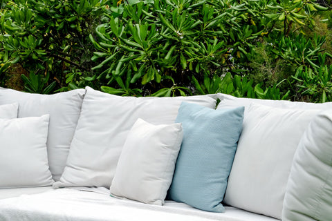 A white couch with blue Pillow Factory Euro Square Pillows and plants in the background.