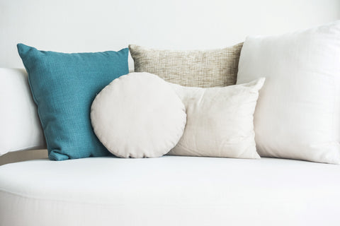 An array of decorative throw pillows with Pillowtex White Duck Feather & Down pillow inserts in blue, beige, and white hues, artfully arranged on a crisp white sofa, creating a serene and inviting ambiance in a modern living space.