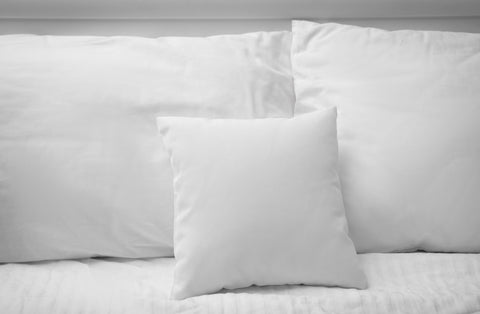 A monochrome scene of a neatly made bed with crisp white linens, featuring a Pillowtex Pillow Insert | White Duck Feather & Down at the center flanked by two others against the headboard, inviting a sense of.