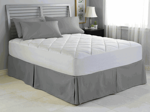 A neatly made bed with a Spring Air Illuna Plush Comfort Mattress Pad, gray bedskirt, and matching pillows in a serene bedroom with a white and gray color scheme, complemented by soft