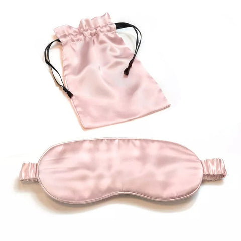 A 100% Mulberry silk sleep eye mask with matching drawstring pouch, featuring soft, ruffled edges and black elastic bands, arranged on a white background for a serene sleep accessory display. (Brand Name: Pillows.com)