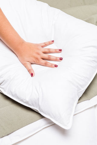 A woman's hand rests on a white pillow filled with DOWNLITE Cambric Eco Cluster Pillow by Downlite.