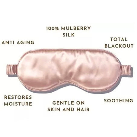 A Mulberry Silk Sleep Eye Mask from Pillows.com in blush pink, boasting anti-aging properties, total blackout for sleep enhancement, moisture restoration, and a gentle, soothing touch on both skin and hair.