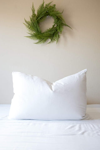 A white Creative Bedding Fossfill Pillow rests on a bed adorned with a fern wreath.