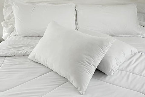 A neatly made bed with crisp white bedding and multiple fluffy pillows, showcasing a cozy and inviting sleeping arrangement that includes Encompass Group 50/50 White Goose Feather & Down Pillows for a Sleep Better Guarantee.