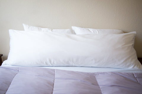 A Pillowtex Premium Polyester Body Pillow resting on a purple comforter.