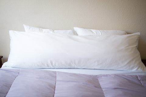 A Pillowtex White Goose Feather and Down Body Pillow resting on a purple comforter.