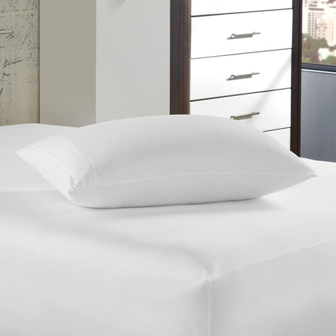 A plush white pillow with a PureCare OmniGuard Pillow Protector rests on a neatly made bed with crisp white linens, against the backdrop of a modern bedroom with a stylish dresser, ensuring protection from allergens.