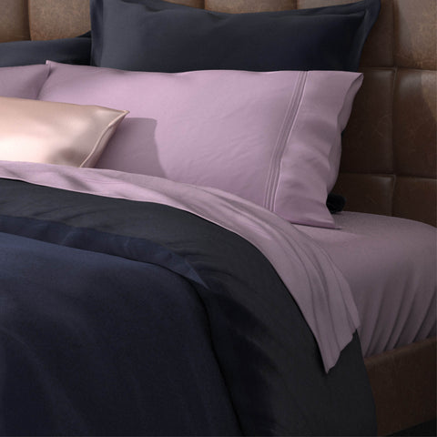 A bed with purple, blue, and black pillows topped with PureCare Premium Bamboo Sheet Sets.