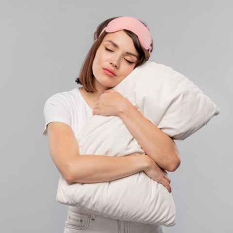 A young woman is sleeping on a gray background while holding a Hollander Eco-Smart Down Alternative Pillow made from recycled materials.
