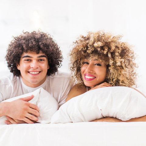 A man and woman relaxing on a bed with DOWNLITE Primaloft Down Alternative Pillows from Downlite.