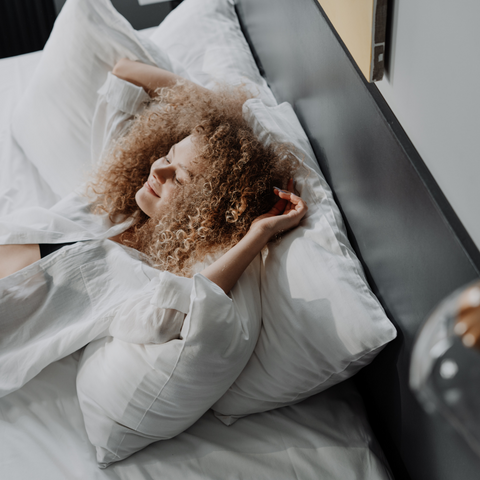 A woman with curly hair is laying in bed on an Envirosleep Gold Pillow featured at many hotels by Manchester Mills.