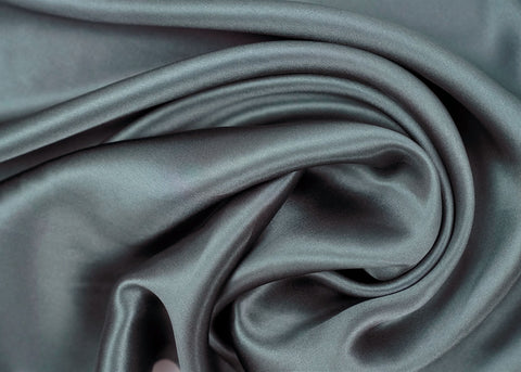 Luxurious dark gray 16 momme silk fabric with an elegant sheen, gracefully draped with soft folds and curves, showcasing its smooth, silky texture ideal for hair and skin care as a Pillowtex 100% Mulberry Silk Pillowcase | Zipper Enclosure, 16 Momme.