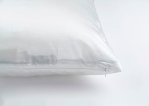 A plain white 16 momme Pillowtex 100% Mulberry Silk pillowcase with a subtle sheen, featuring a neatly sewn corner and a small zipper closure, rests against a soft, light background.