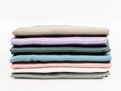silk pillowcases stacked showing color options fawn, lavender, slate,  blue, dustry rose, white, and gray