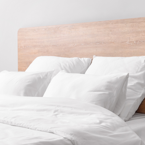 A white bed with The Pillow Factory Housekeeper's Choice Platinum Pillows and a wooden headboard.