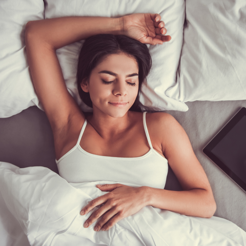 A woman is laying in bed with a Pillowtex® Premium Polyester Pillow supporting her as she uses a tablet.