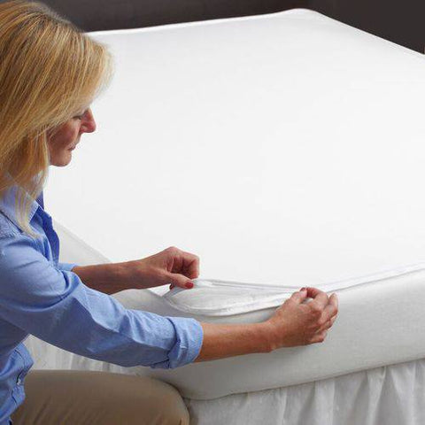 A woman carefully placing a PureCare OmniGuard Total Mattress Protector on her bed to shield against allergens.