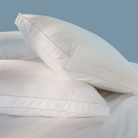 Two Restful Nights Comfort Edge Pillows on top of a bed with a comfortable edge and a blue background.