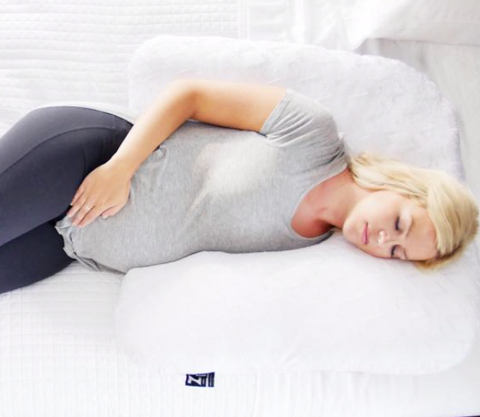 A pregnant woman resting on a Malouf Horseshoe Pillow to alleviate pregnancy discomfort.
