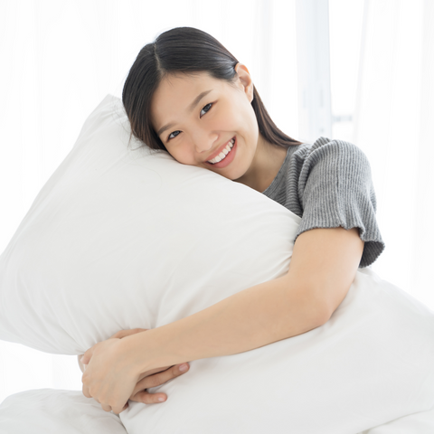A young Asian woman cuddling a Pacific Coast Feather Tria Down & Feather Pillow on a bed at the Ritz-Carlton.