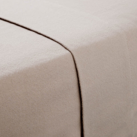 A close-up of a bed with a beige Malouf Portuguese Flannel Sheet Set for a luxurious feel.