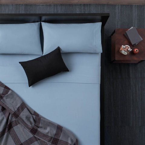 A bed with Malouf Portuguese Flannel Sheet Set and a plaid blanket for a luxurious feel.