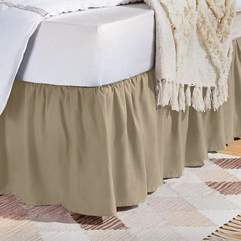 A neatly draped Pillowtex bed skirt, concealing under-bed storage, complements a white sheet, contrasting with a textured throw blanket and lying atop a geometric-patterned area rug, creating a cozy and.