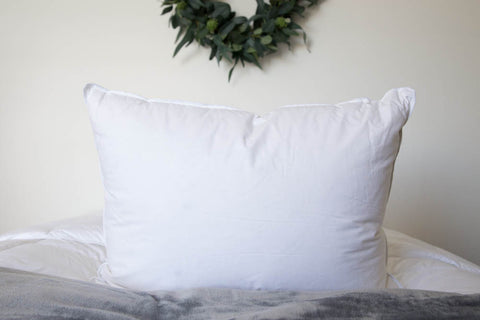 A Down Etc. Luxury Goose Down Pillow | Medium Support on a bed with a wreath on it.