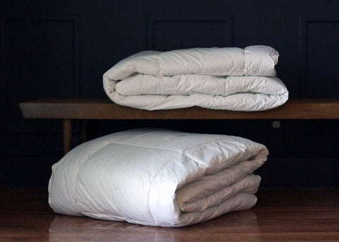 Two white blankets - one Down Etc. Aquaplush Comforter and one Down Etc. - resting on a wooden bench.