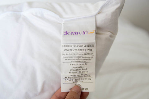 A person holding a Down Etc. Luxury Goose Down Pillow | Medium Support with a label on it.