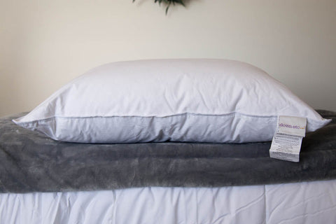 A Down Etc. Luxury Goose Down Pillow | Medium Support with a label on top of a bed.