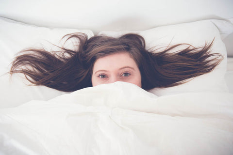 A woman is laying in bed with her head under the duvet, surrounded by Keeco's Choice Hotels® Soft and Firm Polyester Pillow Combo Pack (Includes 2 Pillows).