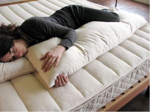 A woman laying on top of a mattress with a Holy Lamb Organics Body Pillow for added support.
