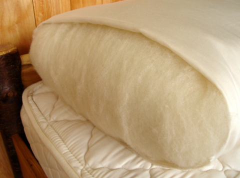 An Holy Lamb Organics Wool-Filled Bed Pillow on top of a wooden bed.
