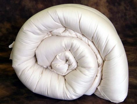 A tightly rolled Holy Lamb Organics Natural Quilted Topper - Ultimate Topper Thickness, featuring an eco-wool filling, presents a spiral reminiscent of a seashell, providing a visual comparison to natural forms, while offering a sense of softness.