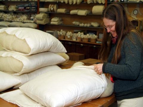 A woman is placing a Holy Lamb Organics Natural Quilted Topper - Ultimate Topper Thickness on a table.