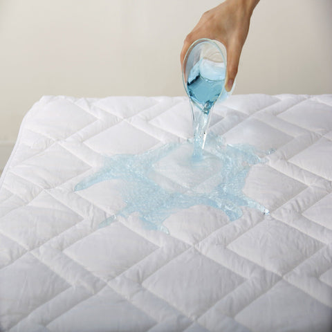 A person pouring a liquid onto a Down Etc. Lily-Pad Waterproof Mattress Pad.